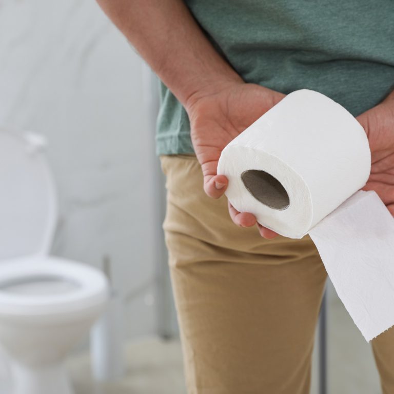Man with toilet paper suffering from hemorrhoid in rest room, closeup
